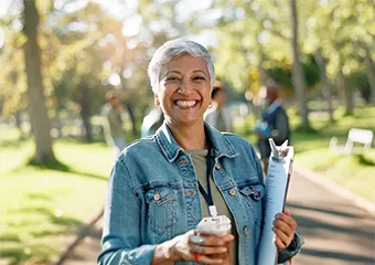 A woman smiling to the camera with a cup of coffee on her hand