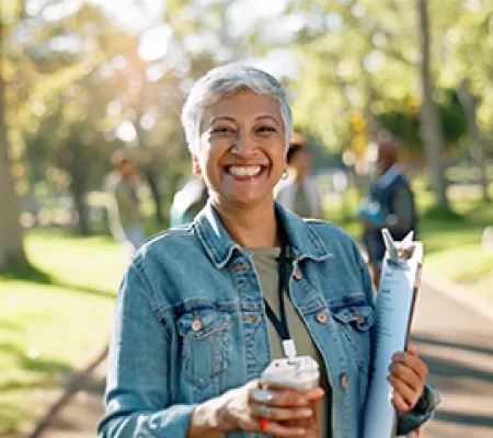 A woman smiling to the camera with a cup of coffee on her hand