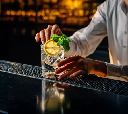 a photo showing a man hand preparing a glass of sparkling water with lemon and mint leaves
