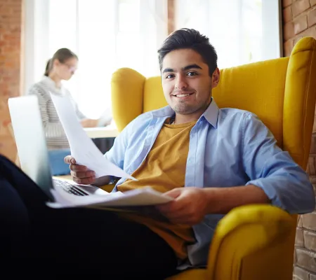 A young man holding a paper in front a laptop
