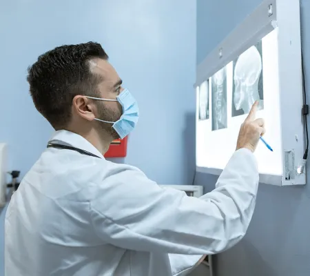 A doctor wearing a mask, checking a skull x-ray.