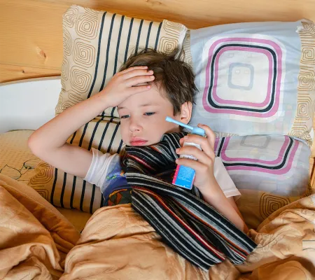 A kid laying on a bed with an inhaler in his hand 