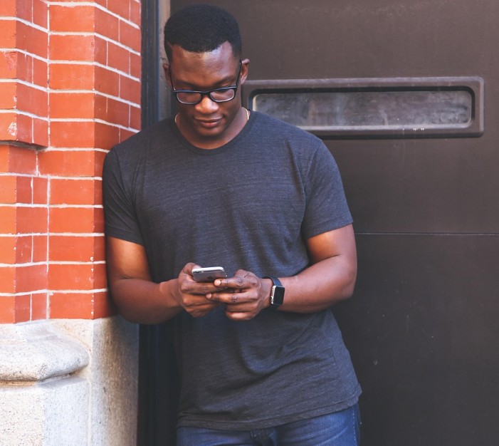 A man looking at his cellphone standing in front a door