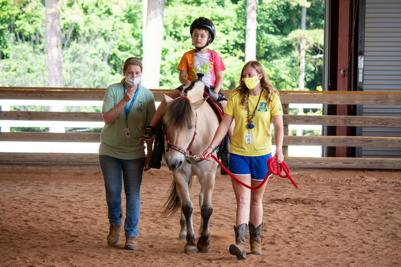 A kid riding a horse with an instructor on the side