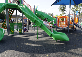 a woman going down on a green slide at the playground